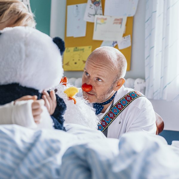 Hospitalsklovnen Baroli sidder ved siden af en hospitalsseng med et barn, som har brækket armen