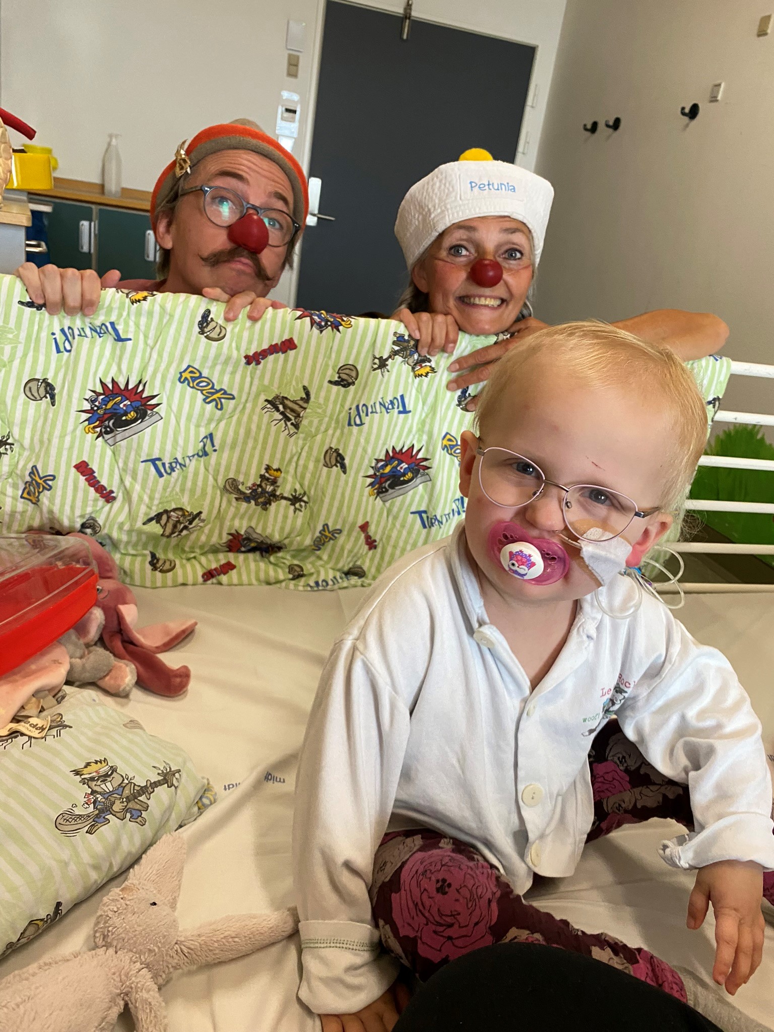 Agnes i en hospitalseng og hospitalsklovnene Turbo og Petunia som kigger på hende