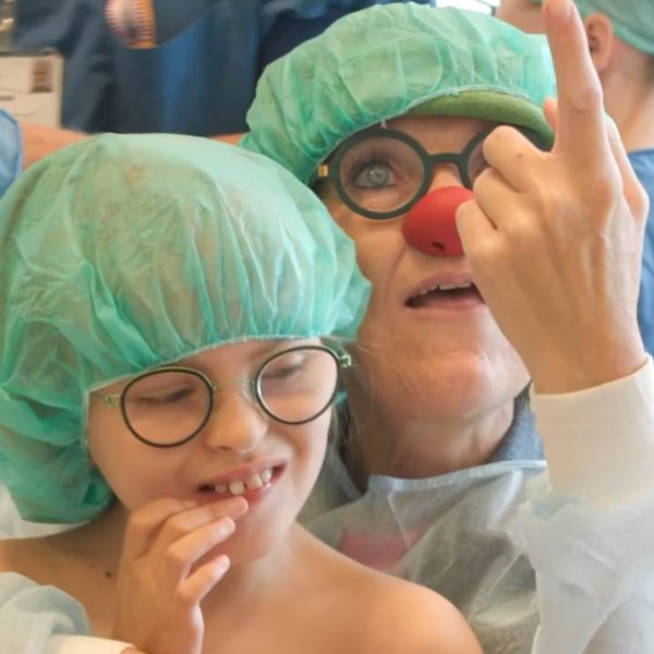 Jonathan og hospitalsklovnen Luna i operationsforberedelse, iført grønne operationshuer – Luna peger op og får Jonathan til at smile.
