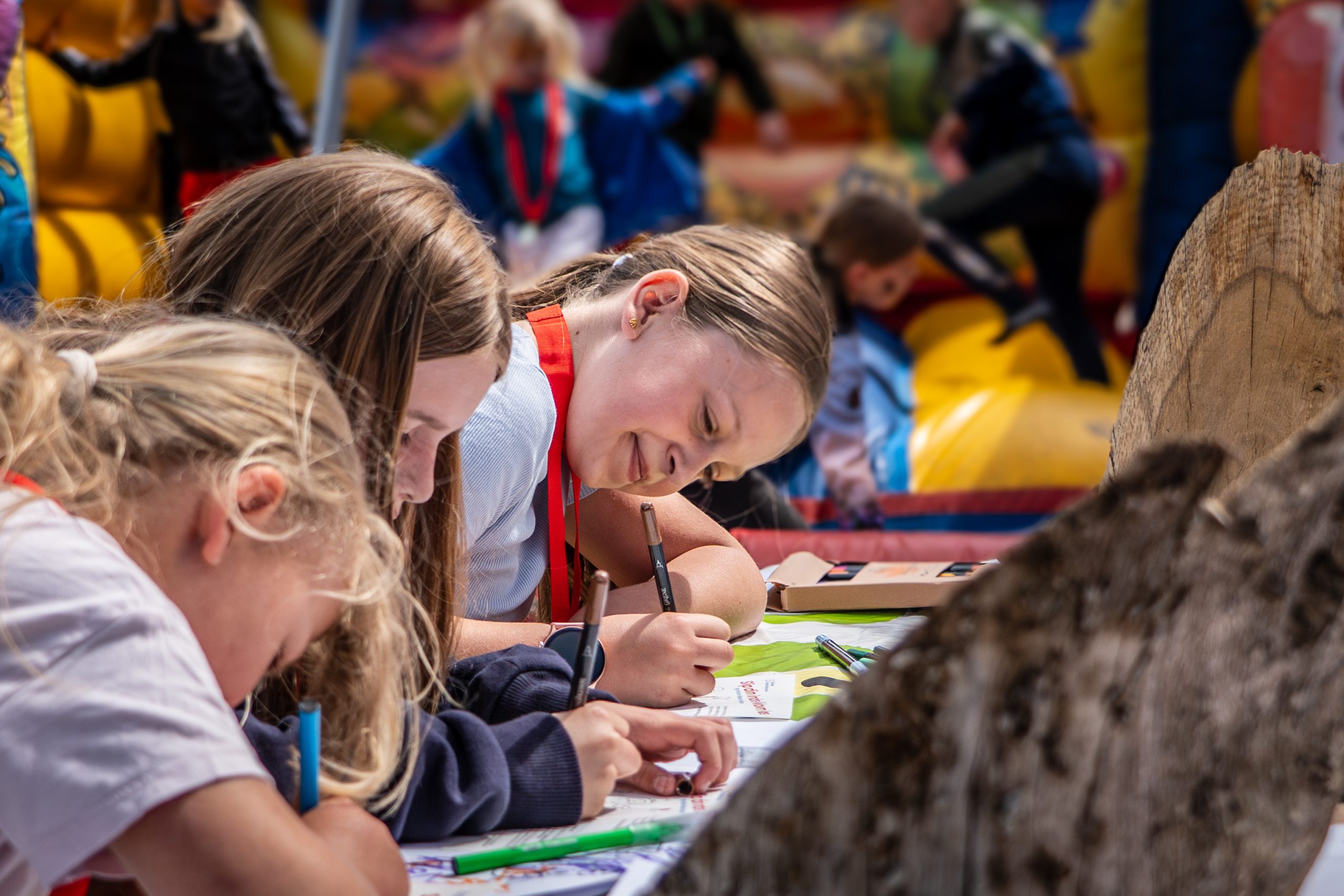 Pernille og Sidney hænger plakater op til Klovneløb. De står foran en rød mur og smiler til hinanden, mens de hænger en gul plakat op.