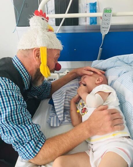 Billede af en klovn og en lille dreng i en seng på hospitalet
