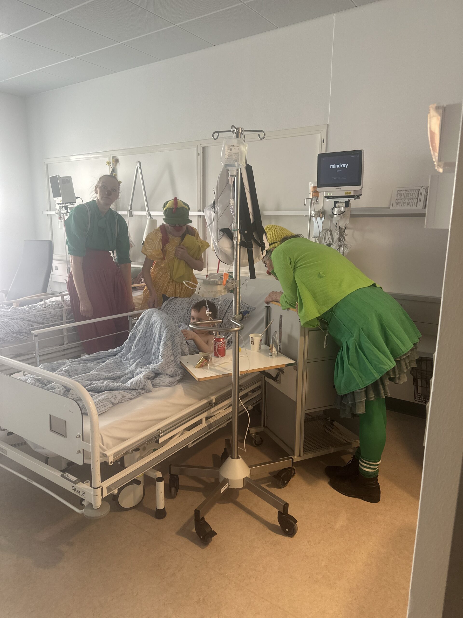 Cebastian ligger i en hospitalsseng med tre hospitalsklovne omkring sig